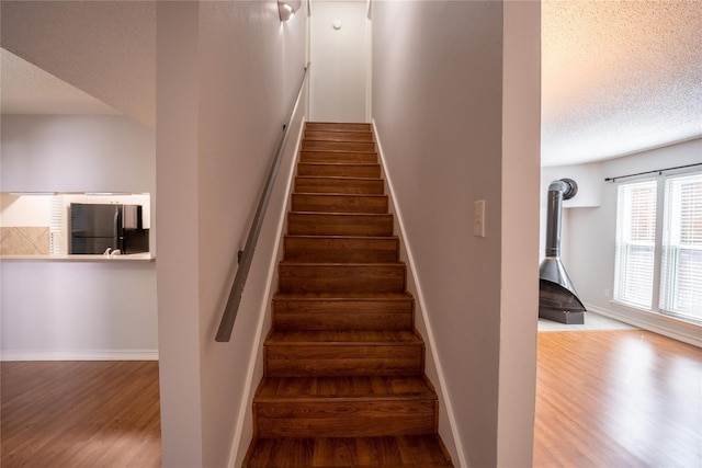 staircase with hardwood / wood-style flooring, a wood stove, and a textured ceiling