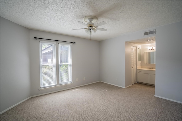 unfurnished bedroom with sink, ensuite bath, ceiling fan, a textured ceiling, and light colored carpet