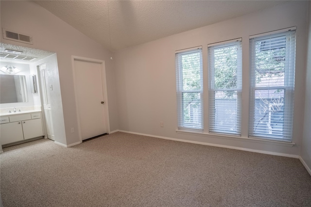 unfurnished bedroom featuring ensuite bathroom, a textured ceiling, light colored carpet, sink, and lofted ceiling