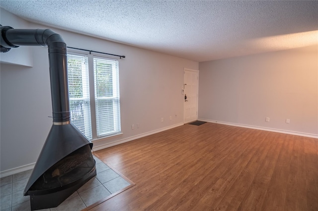 unfurnished living room with a wood stove, wood-type flooring, and a textured ceiling