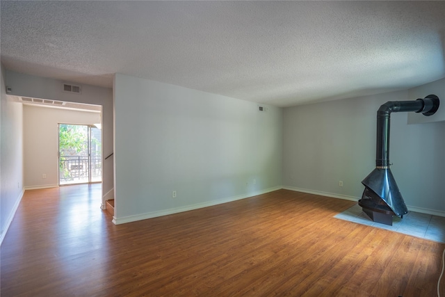 unfurnished living room with hardwood / wood-style floors, a wood stove, and a textured ceiling