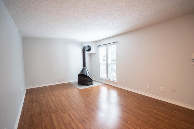 unfurnished living room with a wood stove, wood-type flooring, and a textured ceiling