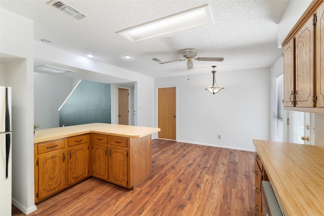 kitchen featuring white fridge, wood-type flooring, a textured ceiling, and kitchen peninsula