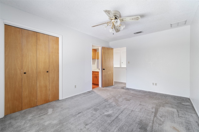 unfurnished bedroom featuring ceiling fan, a textured ceiling, a closet, light colored carpet, and ensuite bath