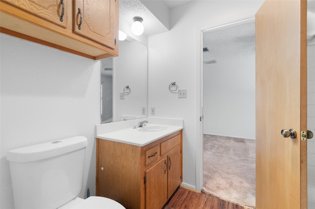 bathroom with a textured ceiling, hardwood / wood-style floors, vanity, and toilet