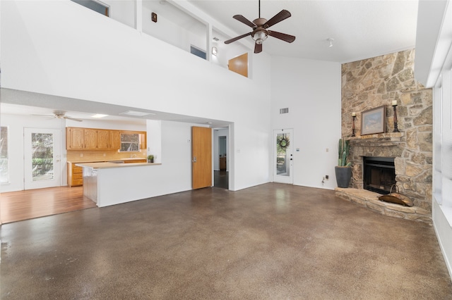 unfurnished living room with a towering ceiling, ceiling fan, and a stone fireplace