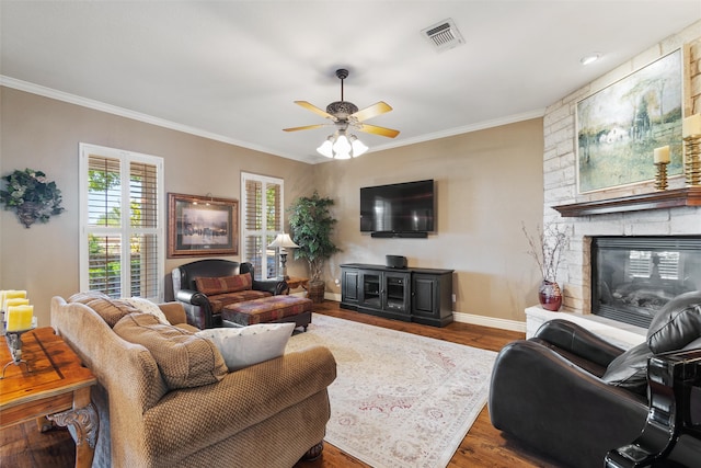 living room featuring wood-type flooring, a stone fireplace, ceiling fan, and ornamental molding