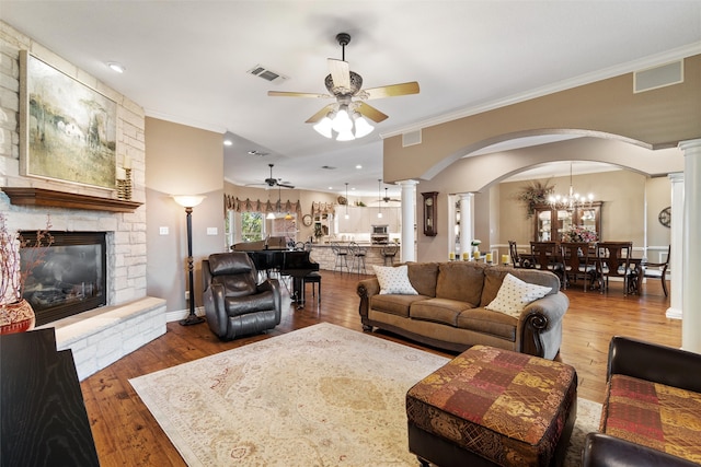 living room with wood-type flooring, ceiling fan with notable chandelier, ornate columns, and ornamental molding