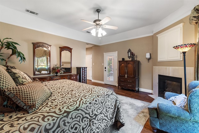 bedroom featuring a tiled fireplace, ceiling fan, dark hardwood / wood-style flooring, and access to exterior