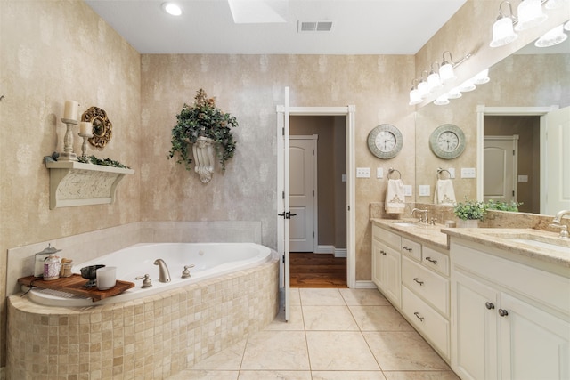 bathroom featuring tile patterned floors, vanity, tiled tub, and a skylight