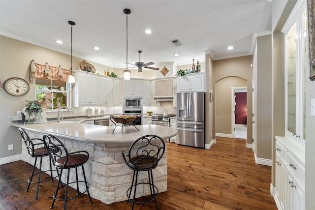 kitchen featuring appliances with stainless steel finishes, dark hardwood / wood-style flooring, tasteful backsplash, white cabinetry, and a breakfast bar area