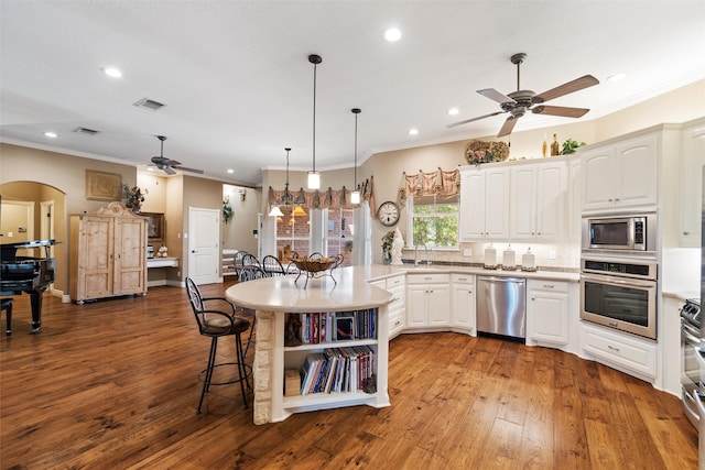 kitchen featuring hanging light fixtures, appliances with stainless steel finishes, a breakfast bar area, white cabinets, and hardwood / wood-style flooring