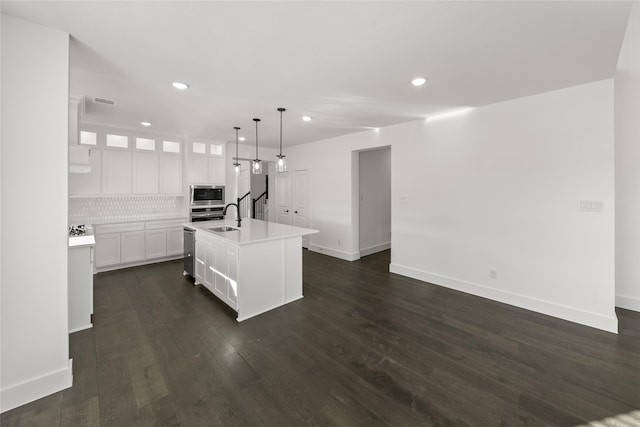 kitchen featuring pendant lighting, white cabinets, stainless steel appliances, an island with sink, and decorative backsplash