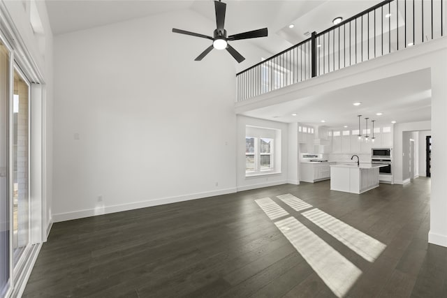 unfurnished living room with sink, ceiling fan, high vaulted ceiling, and dark wood-type flooring