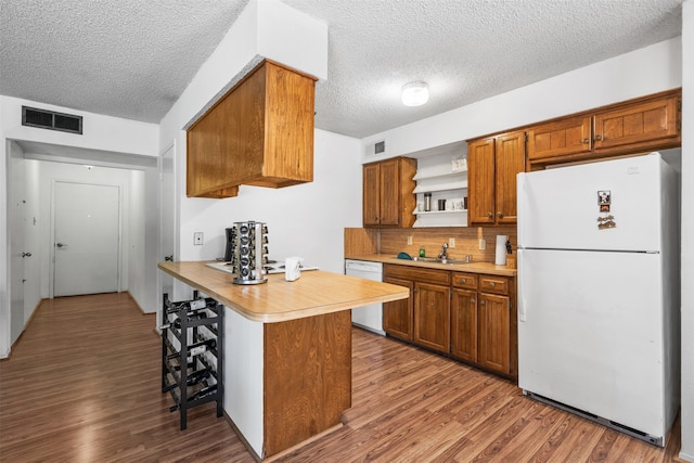 kitchen featuring hardwood / wood-style flooring, kitchen peninsula, a kitchen bar, and white appliances