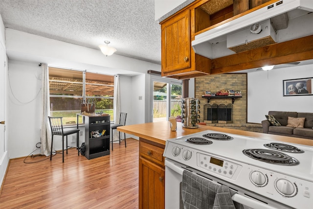 kitchen featuring a brick fireplace, light hardwood / wood-style floors, white range with electric cooktop, and a textured ceiling