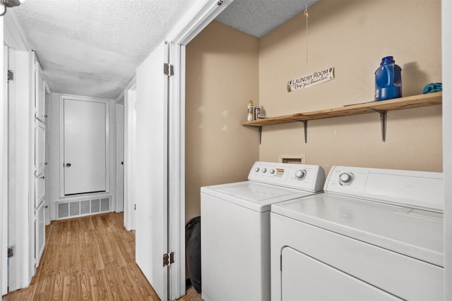 laundry room with light wood-type flooring, a textured ceiling, and washer and dryer