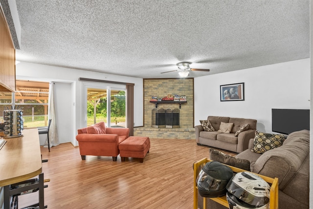 living room featuring ceiling fan, a textured ceiling, light wood-type flooring, and a fireplace