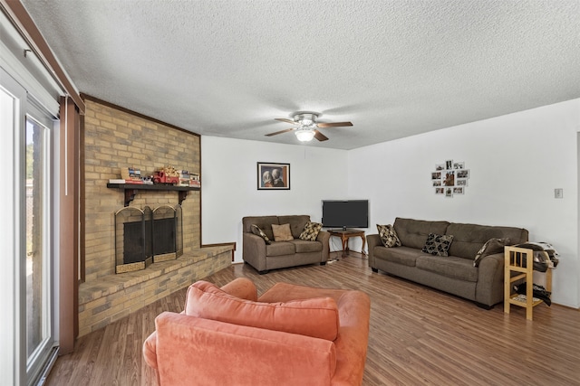 living room with a textured ceiling, ceiling fan, dark wood-type flooring, and a brick fireplace