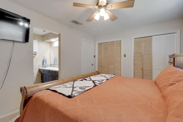 bedroom featuring two closets, ensuite bath, ceiling fan, and carpet