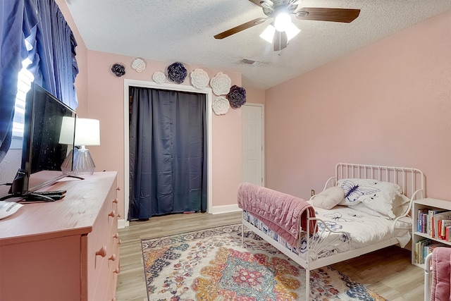 bedroom with a textured ceiling, light hardwood / wood-style floors, and ceiling fan