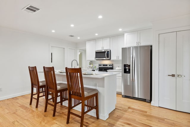 kitchen with light wood-type flooring, an island with sink, white cabinetry, a kitchen breakfast bar, and stainless steel appliances