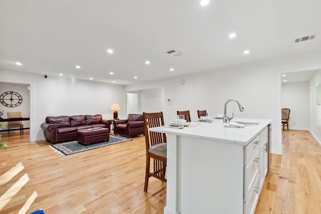 kitchen with white cabinets, sink, a kitchen island with sink, light wood-type flooring, and a kitchen bar