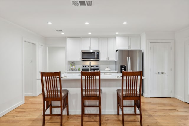 kitchen featuring light hardwood / wood-style floors, a breakfast bar area, stainless steel appliances, and white cabinets