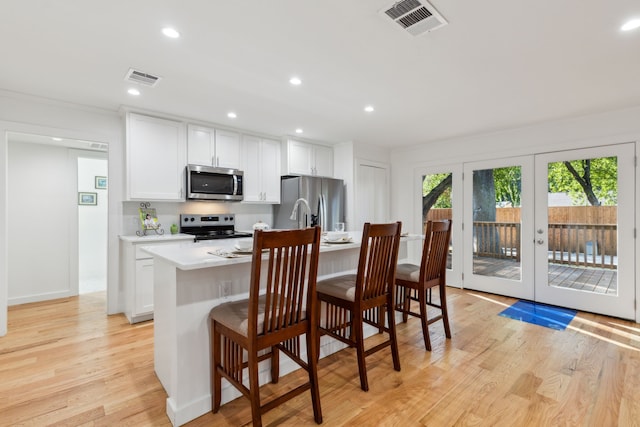 kitchen with an island with sink, white cabinetry, light hardwood / wood-style flooring, and stainless steel appliances