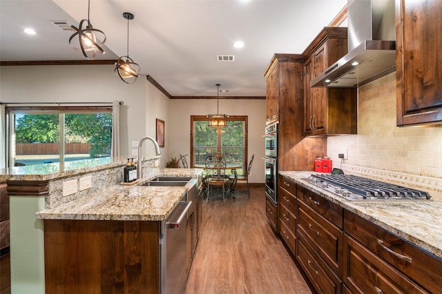 kitchen with wall chimney range hood, sink, crown molding, decorative light fixtures, and light hardwood / wood-style floors