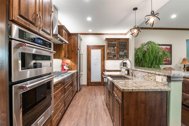 kitchen featuring stainless steel appliances, light stone counters, pendant lighting, decorative backsplash, and light wood-type flooring