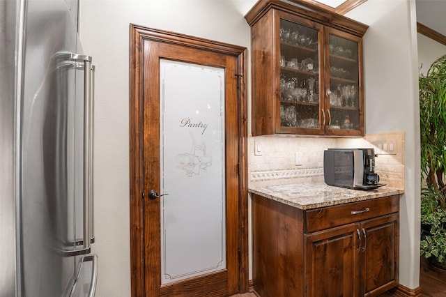 bar with decorative backsplash, high end refrigerator, dark brown cabinetry, and light stone countertops