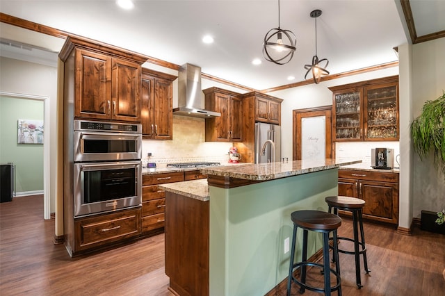 kitchen with light stone countertops, wall chimney exhaust hood, a breakfast bar, stainless steel appliances, and an island with sink