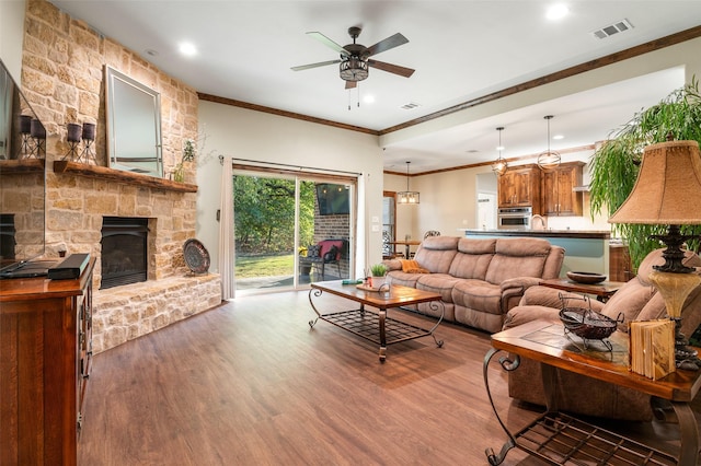 living room with dark hardwood / wood-style floors, ceiling fan, a stone fireplace, and crown molding