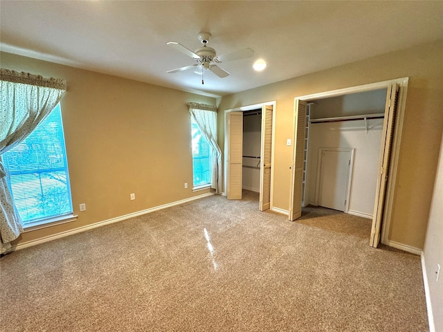 unfurnished bedroom with two closets, ceiling fan, baseboards, and carpet flooring