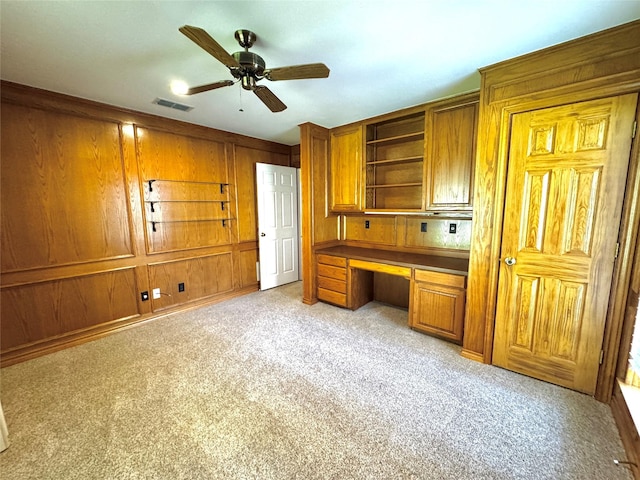 unfurnished office with light carpet, visible vents, built in desk, a ceiling fan, and wooden walls