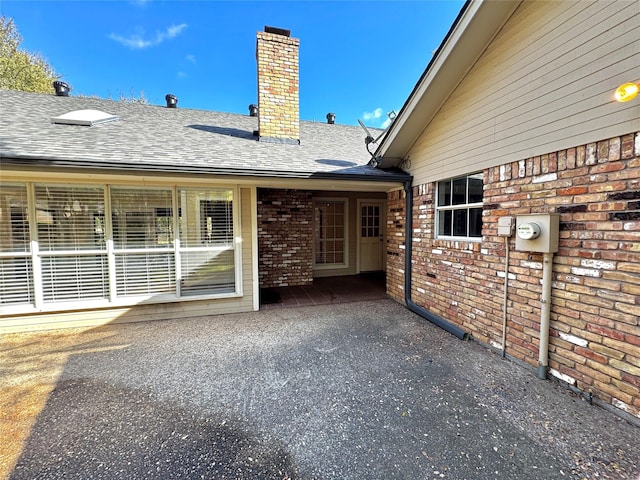 exterior space featuring brick siding, roof with shingles, and a chimney