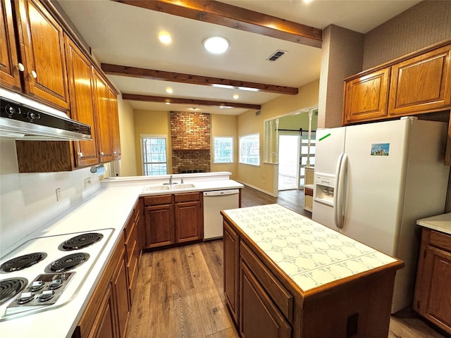 kitchen with a sink, light wood-style floors, white appliances, beamed ceiling, and visible vents