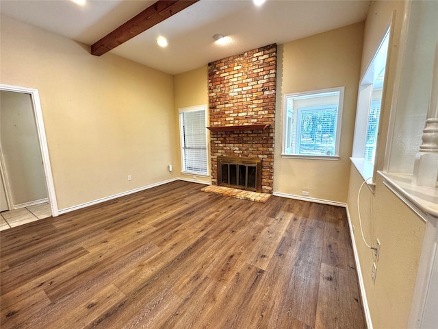 unfurnished living room with beamed ceiling, baseboards, wood finished floors, and a fireplace
