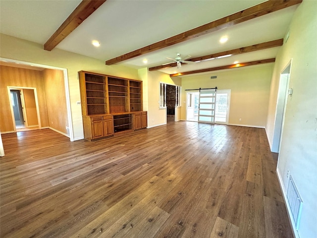 unfurnished living room featuring a barn door, wood finished floors, visible vents, beam ceiling, and baseboards