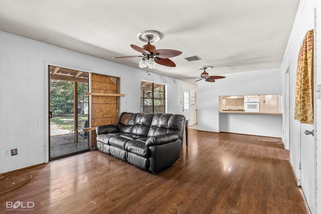 living room with dark wood-type flooring, ceiling fan, and a healthy amount of sunlight