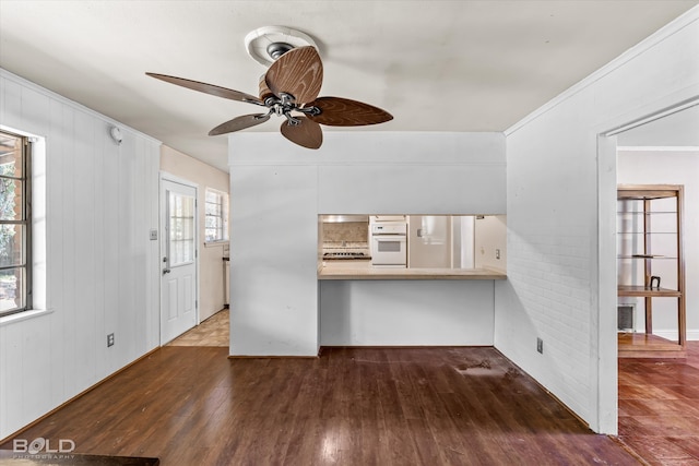 unfurnished living room with wooden walls, dark wood-type flooring, ceiling fan, and a healthy amount of sunlight