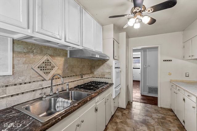 kitchen with white cabinets, sink, backsplash, stainless steel gas stovetop, and white oven