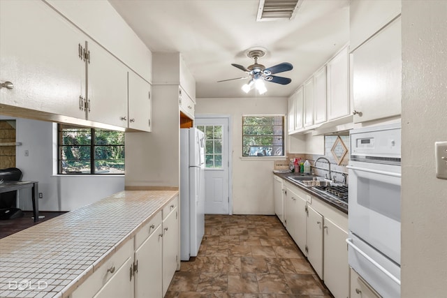 kitchen with white appliances, sink, ceiling fan, and white cabinets