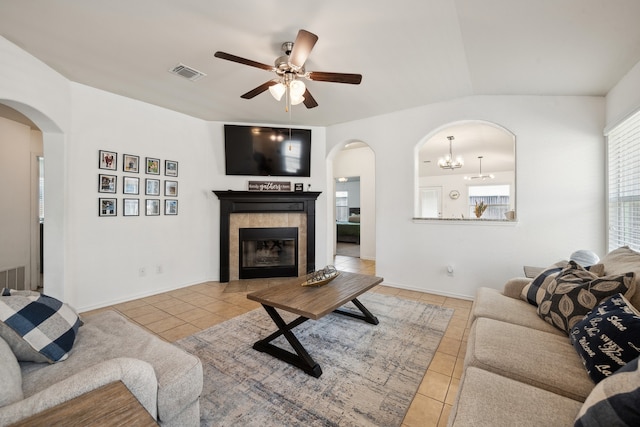 living room with ceiling fan with notable chandelier, lofted ceiling, a tiled fireplace, and light tile patterned floors