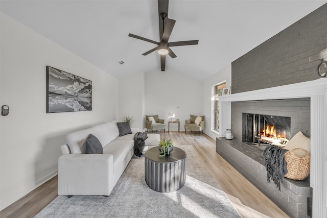 living room featuring ceiling fan, lofted ceiling, light wood-type flooring, and a fireplace