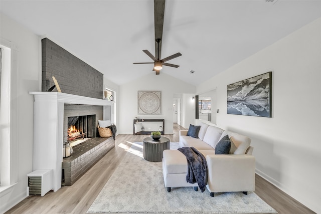 living room with vaulted ceiling with beams, light hardwood / wood-style floors, ceiling fan, and a brick fireplace