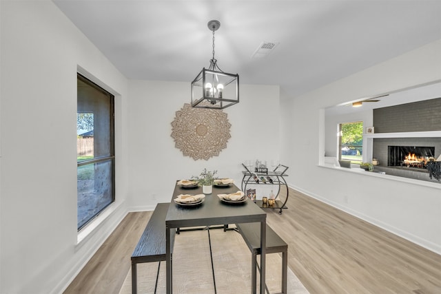 dining area featuring wood-type flooring, a notable chandelier, and a brick fireplace