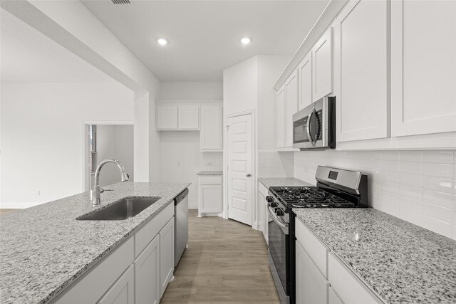 kitchen with stainless steel appliances, backsplash, a center island with sink, white cabinetry, and light hardwood / wood-style floors