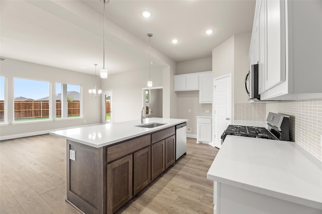 kitchen with sink, light wood-type flooring, stainless steel appliances, pendant lighting, and a center island with sink